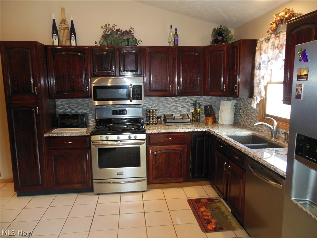 4679 Wood Road Madison, OH 44057 - Photo 9 of 23 Vaulted Kitchen with ceramic floor, granite countertops, glass backsplash, and stainless steel appliances.