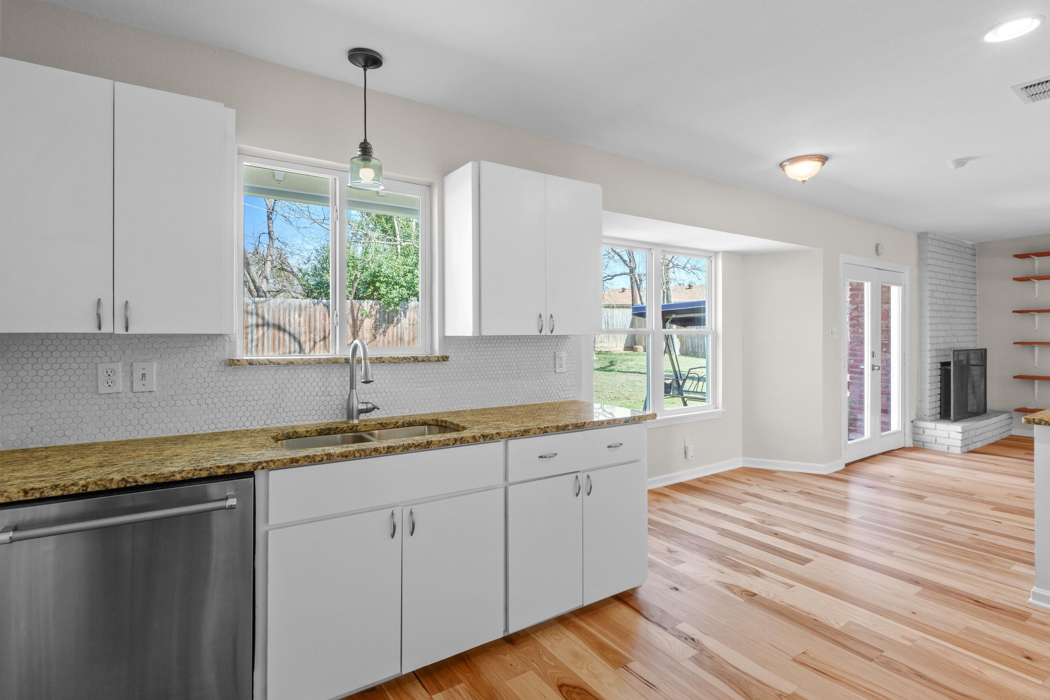 2312 Rogge Lane Austin, TX 78723 - Photo 11 of 34 Kitchen with stainless steel dishwasher, backsplash, white cabinetry, light wood-style floors, and light stone counters.