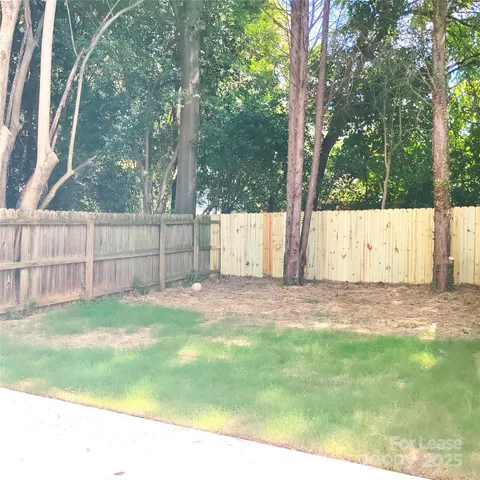 a view of a backyard with large trees and wooden fence
