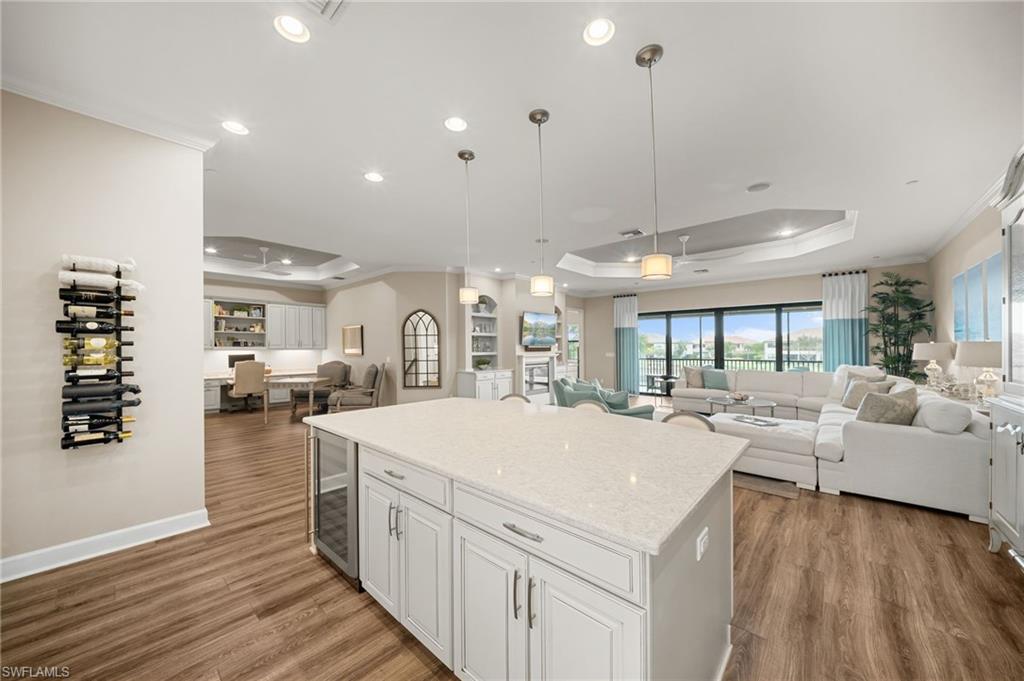 9672 Montelanico Loop, Unit 203 Naples, FL 34119 - Photo 11 of 49 a large white kitchen with kitchen island a stove a sink dishwasher and a fireplace with wooden floor