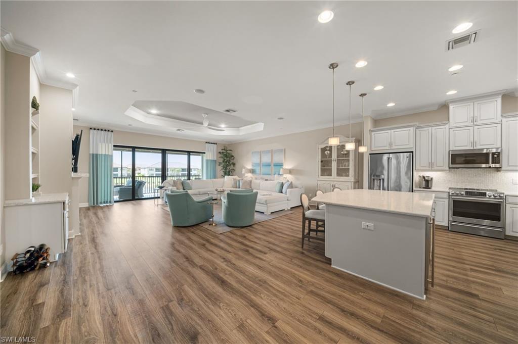9672 Montelanico Loop, Unit 203 Naples, FL 34119 - Photo 4 of 49 a open kitchen with kitchen island a stove a refrigerator a sink dishwasher with a dining table and chairs with wooden floor