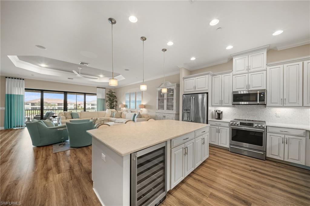 9672 Montelanico Loop, Unit 203 Naples, FL 34119 - Photo 10 of 49 a large kitchen with kitchen island a stove a sink a refrigerator and a dining table with wooden floor