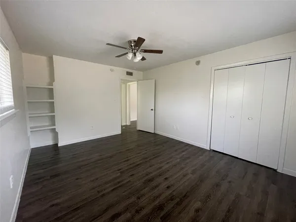 an empty room with wooden floor closet and windows
