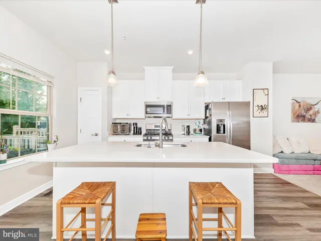 a kitchen with stainless steel appliances a stove a sink a refrigerator a center island and a wooden floor