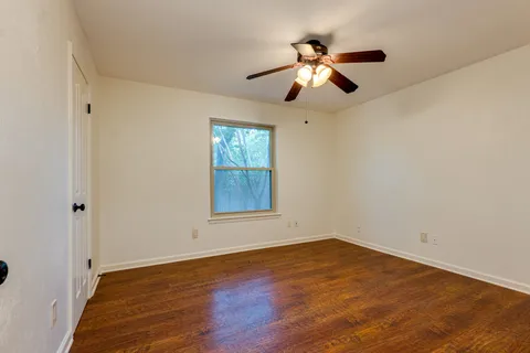 an empty room with wooden floor chandelier fan and windows