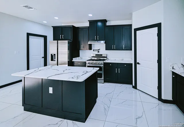 a kitchen with stainless steel appliances kitchen island granite countertop a refrigerator and a stove top oven