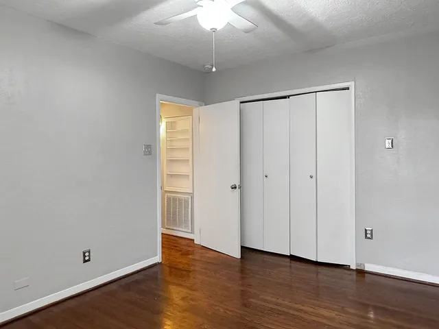 a view of an empty room with wooden floor and a ceiling fan