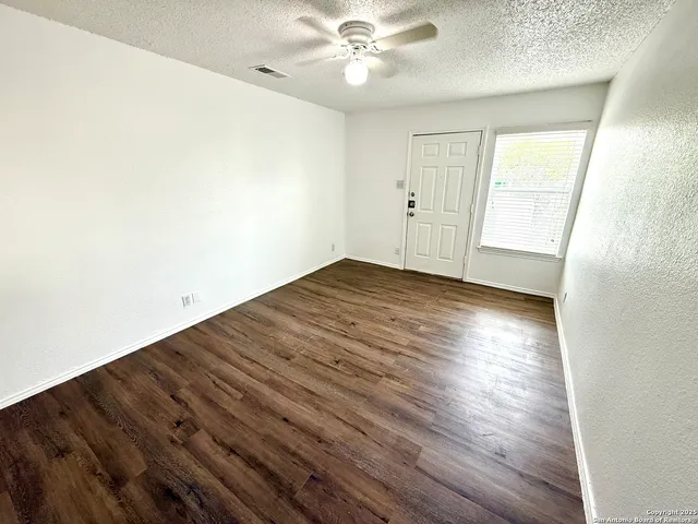 an empty room with wooden floor fan and windows