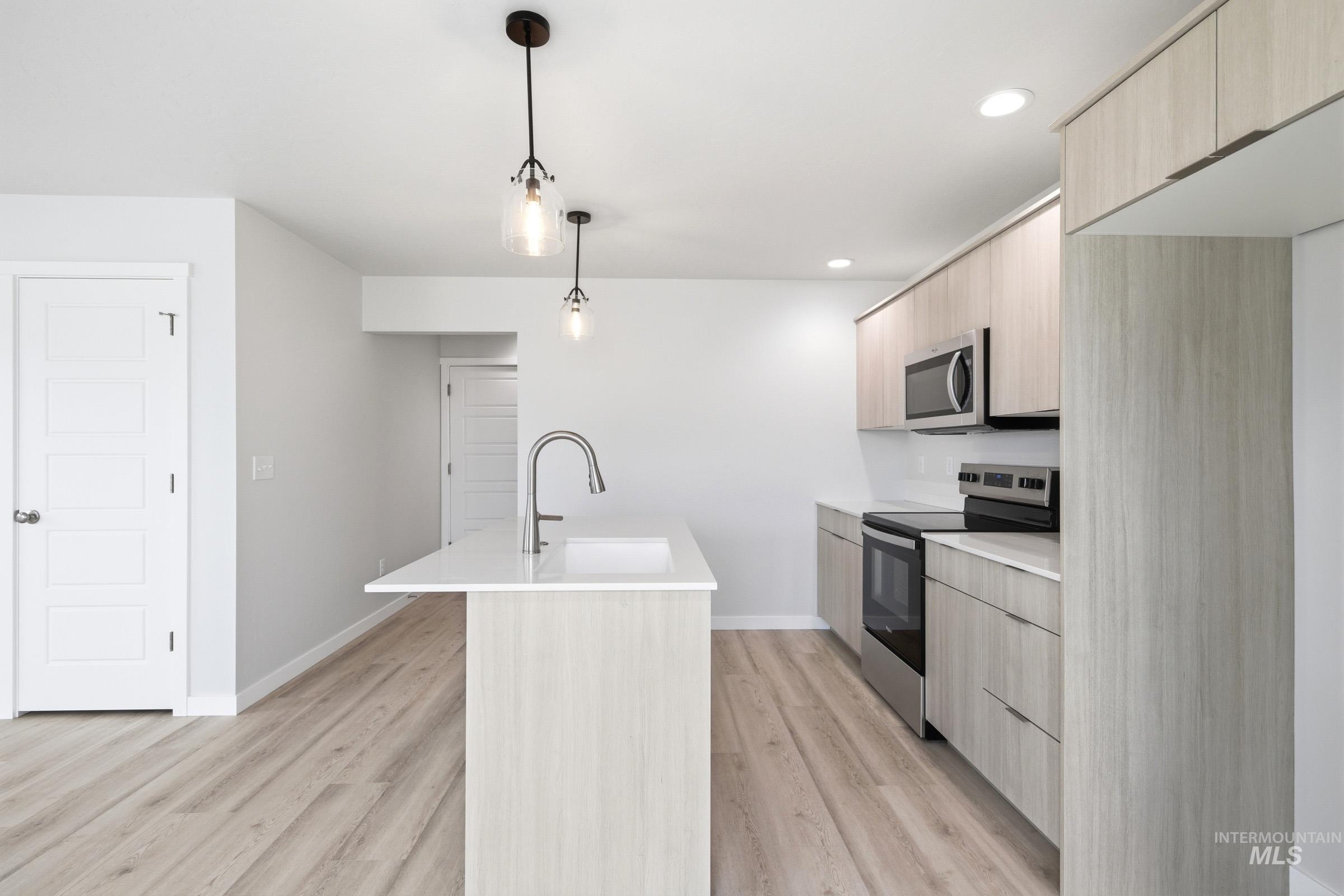 10770 Rutland Street Caldwell, ID 83605 - Photo 3 of 22 Modern kitchen featuring stainless steel appliances, light wood-finish cabinetry, a large center island with a white countertop, and contemporary pendant lighting