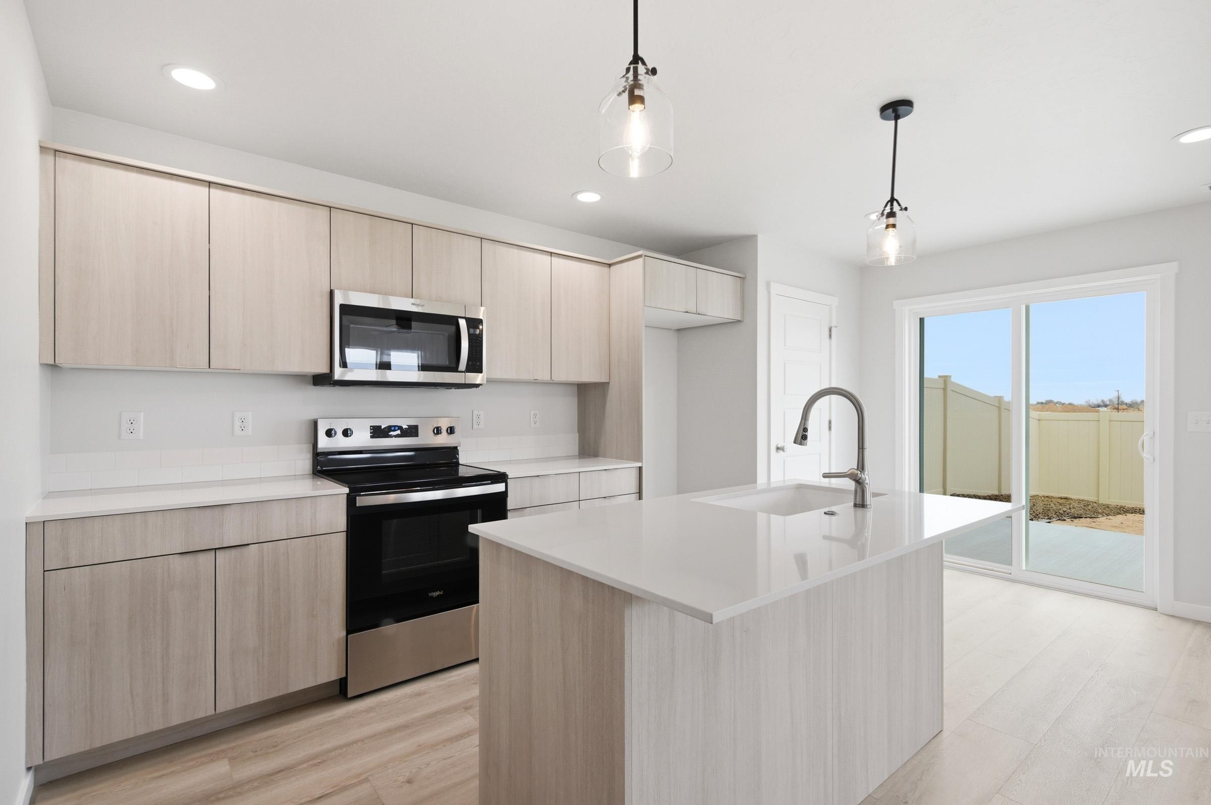 10770 Rutland Street Caldwell, ID 83605 - Photo 4 of 22 Modern kitchen featuring light wood-finish cabinetry, stainless steel appliances, a center island with an integrated sink, and pendant lighting