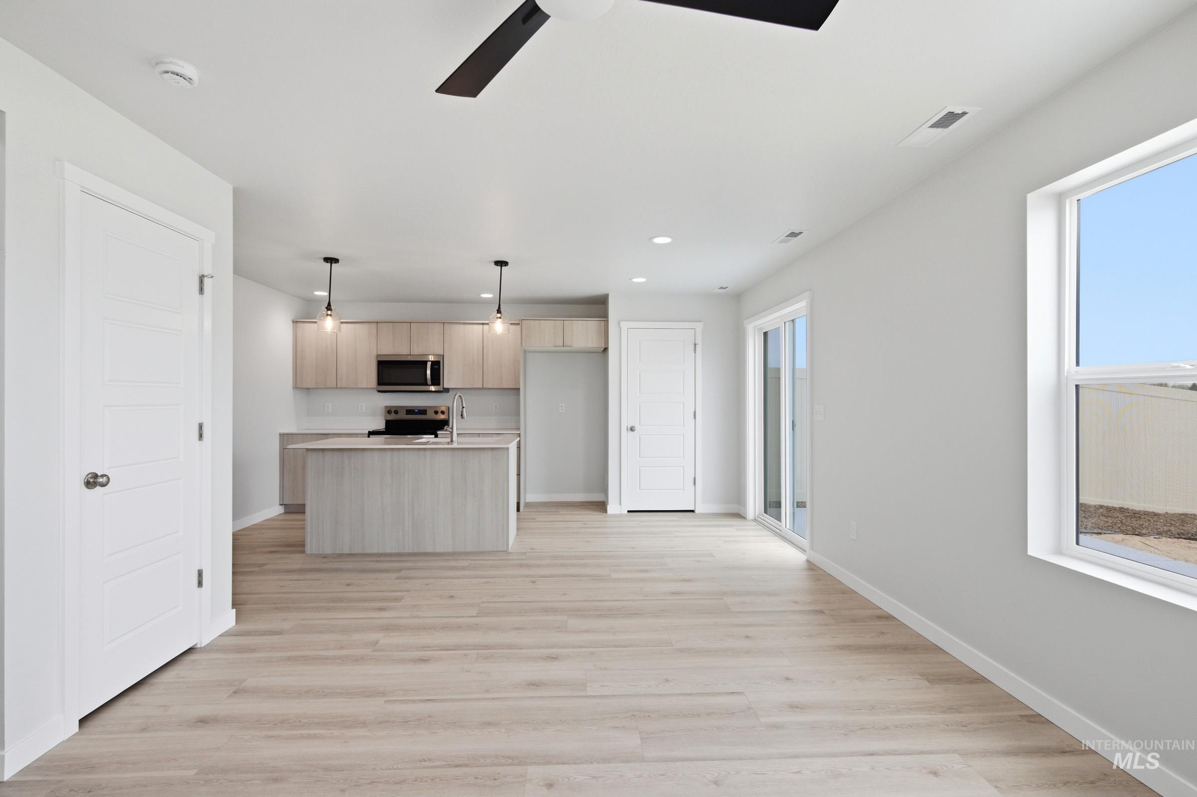 10770 Rutland Street Caldwell, ID 83605 - Photo 8 of 22 Open-concept living area featuring light wood-finish flooring, a contemporary kitchen island with a sink, recessed lighting, and a glass sliding door