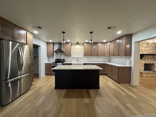 a large kitchen with a center island wooden floor stainless steel appliances and cabinets