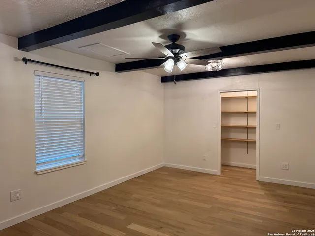 a view of an empty room with a ceiling fan and wooden floor