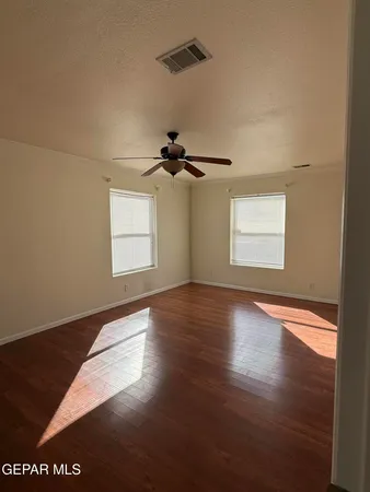 an empty room with wooden floor chandelier fan and windows