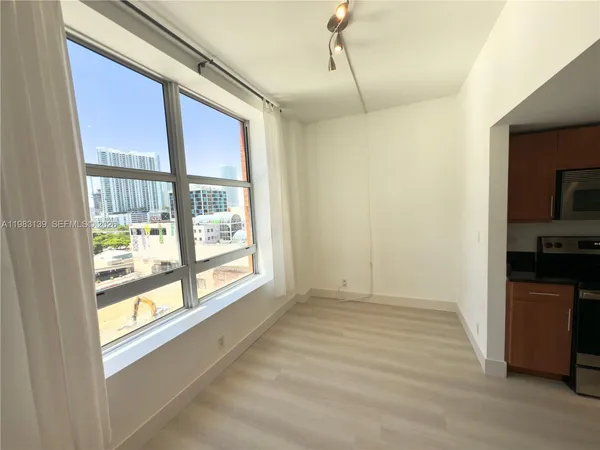 a view of an empty room with a window and a kitchen