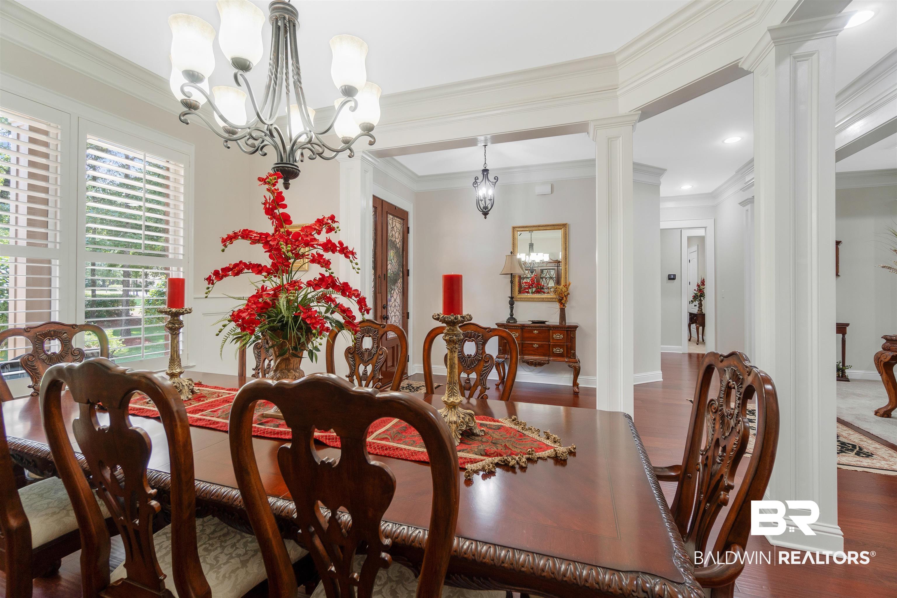 Dining room featuring dark hardwood / wood-style floors, an inviting chandelier, crown molding, and ornate columns