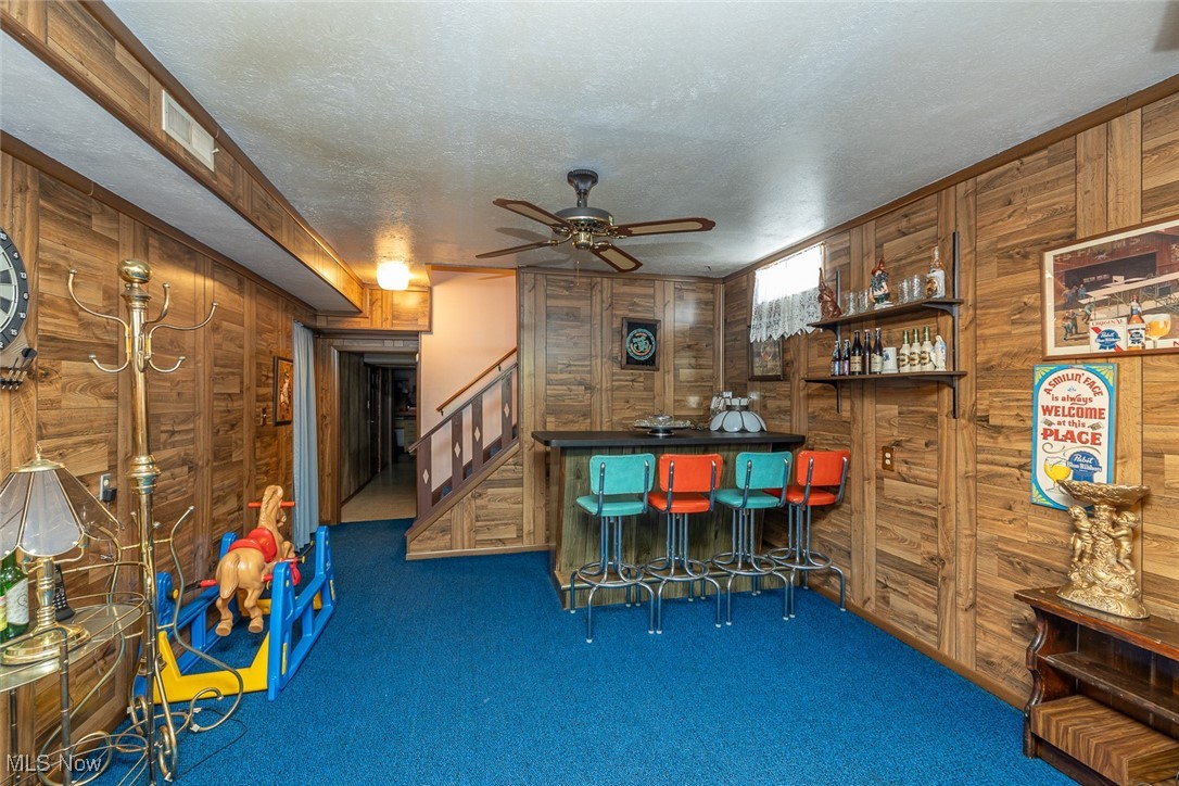 750 Sagamore Road Northfield, OH 44067 - Photo 34 of 37 Bar featuring ceiling fan, a textured ceiling, wooden walls, and dark colored carpet