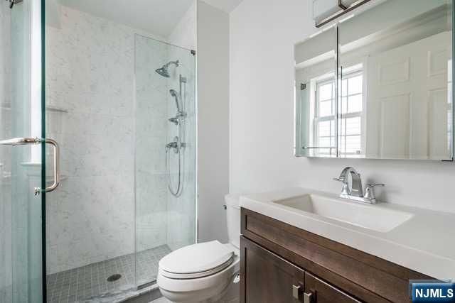 57 71st Street Guttenberg, NJ 07093 - Photo 13 of 18 a bathroom with a sink a toilet a glass door a shower and a window