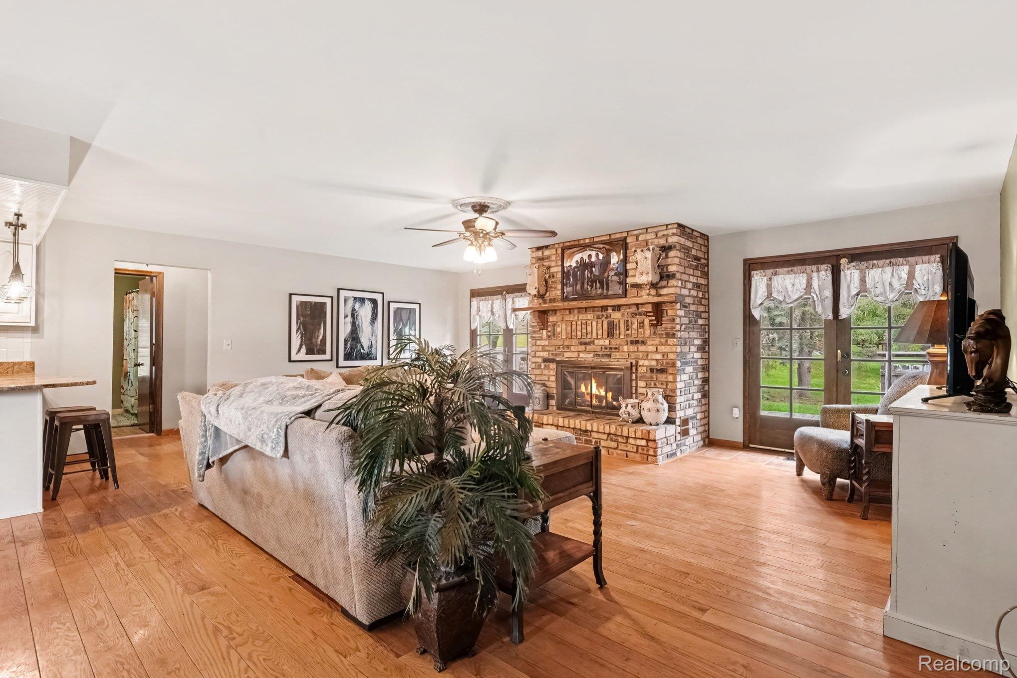 107 Michelle Drive Romeo, MI 48065 - Photo 6 of 30 Spacious living area featuring wood-finish flooring, a brick-surround fireplace with mantel, a ceiling fan, and glass-paneled double doors
