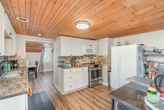 a kitchen with stainless steel appliances granite countertop a stove a refrigerator a sink dishwasher and white cabinets with wooden floor