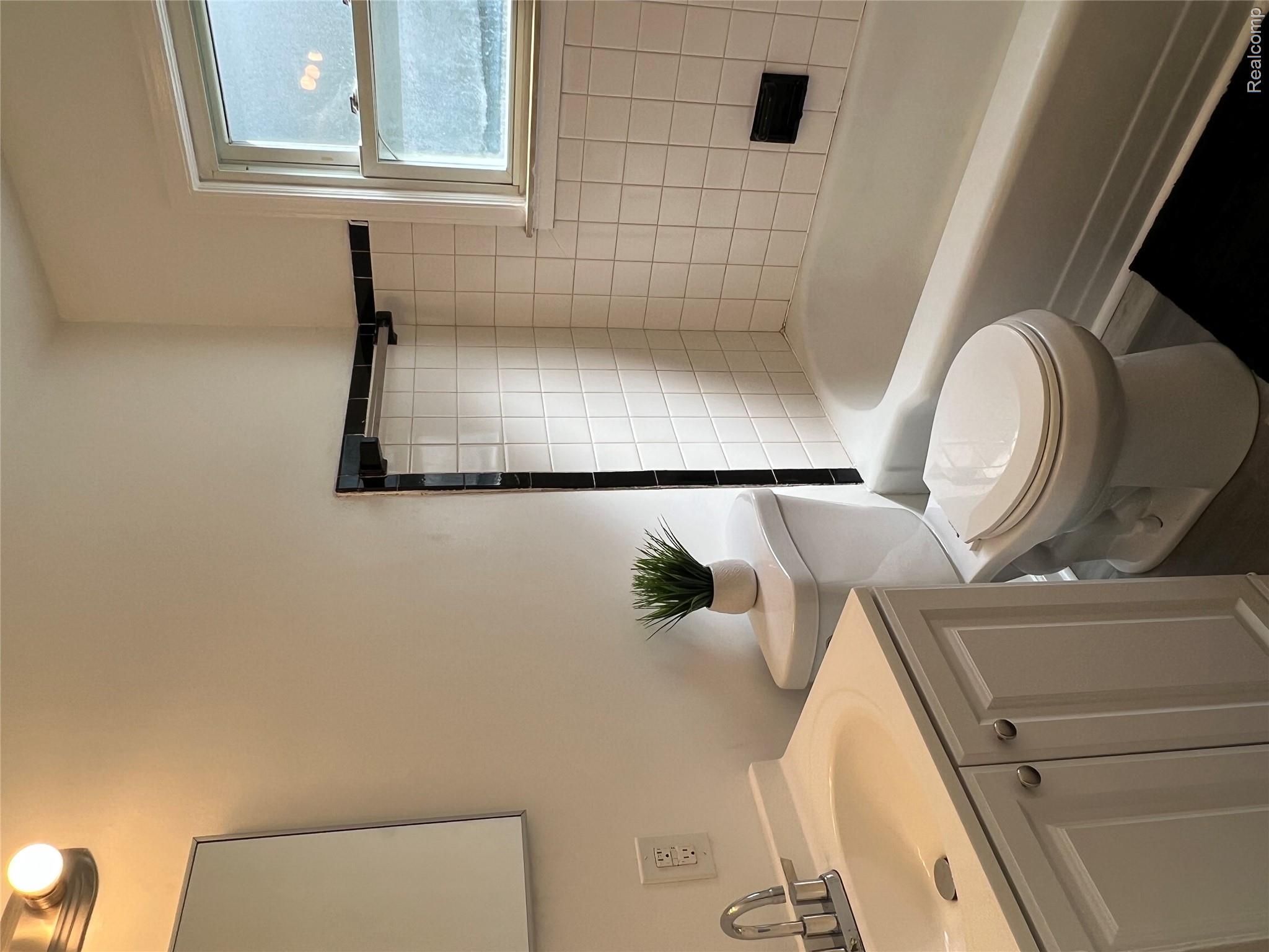 4034 Fleming Road Flint, MI 48504 - Photo 11 of 20 Bathroom featuring a white vanity with cabinet storage, a toilet, a bathtub with white subway tile surround, and a window