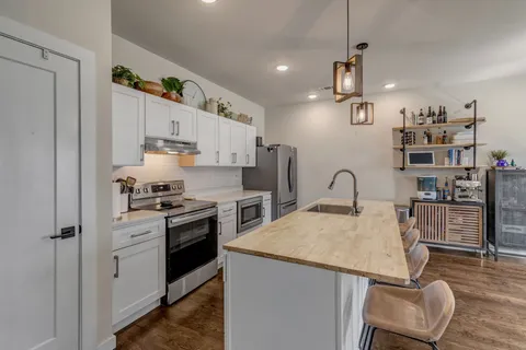 a kitchen with stainless steel appliances granite countertop a refrigerator a stove a sink dishwasher and white cabinets with wooden floor