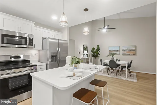 a kitchen with stainless steel appliances kitchen island granite countertop a dining table chairs refrigerator and microwave