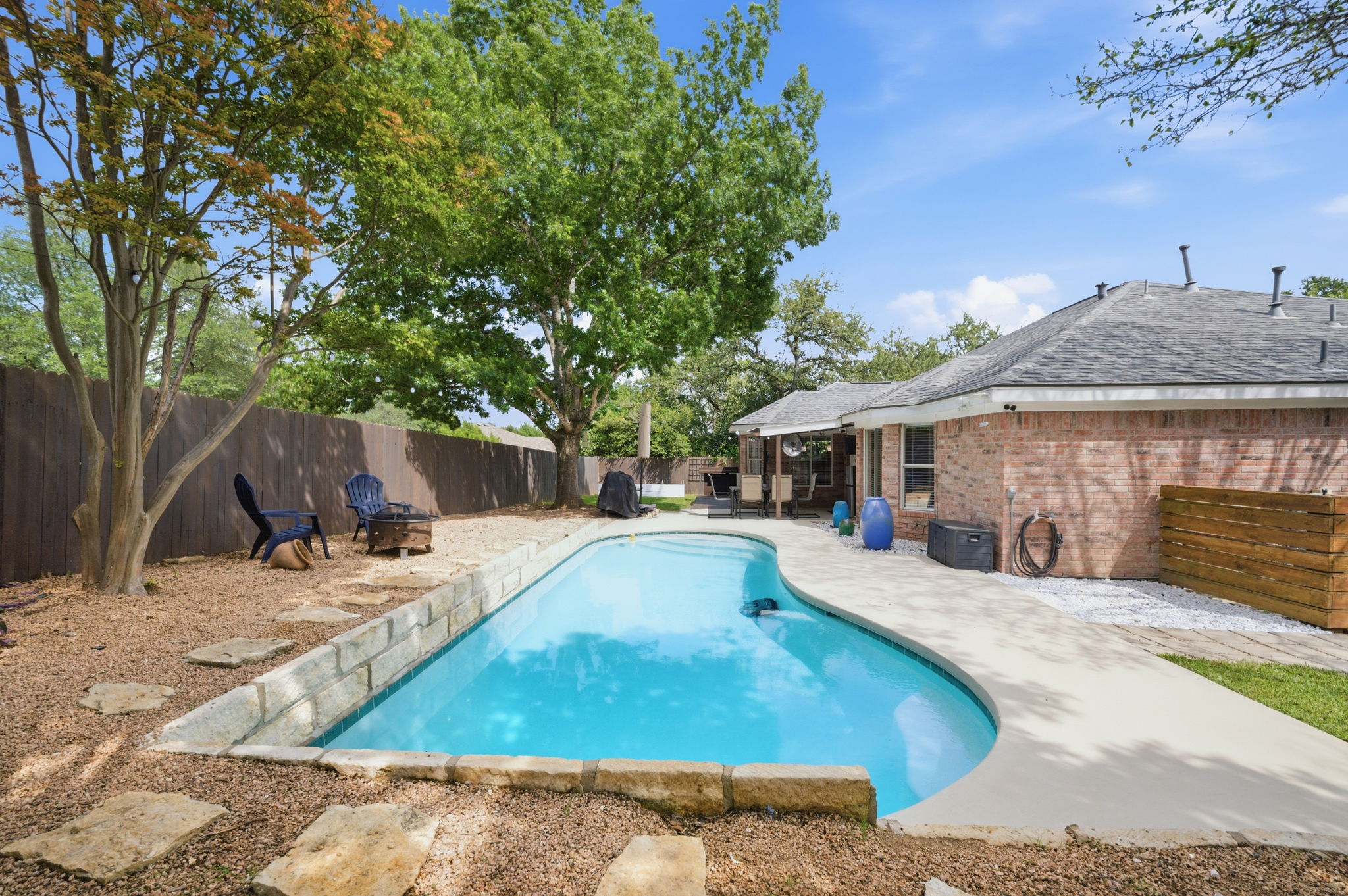 9024 Heiden Lane Austin, TX 78749 - Photo 20 of 28 Backyard oasis featuring a curvilinear swimming pool with concrete coping, a stone block retaining wall, and a surrounding concrete patio