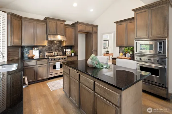 a kitchen with kitchen island granite countertop a stove top oven a sink dishwasher a dining table and chairs with wooden floor