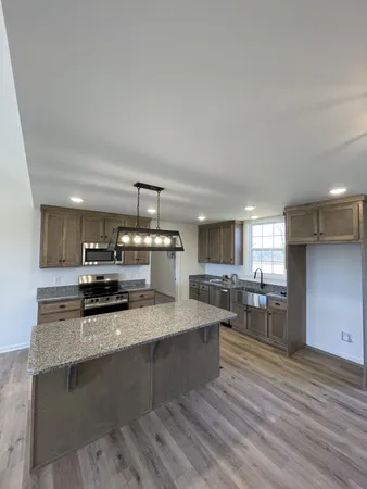 a kitchen with stainless steel appliances granite countertop wooden cabinets a stove top oven a sink dishwasher and wooden floor