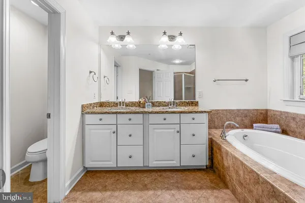 a bathroom with a granite countertop double vanity sink mirror bathtub and toilet