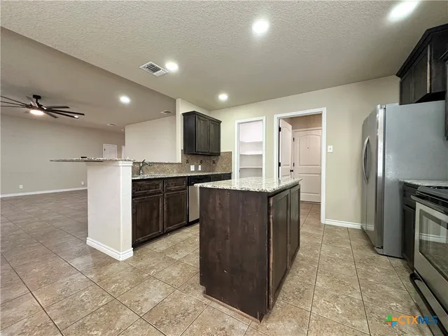 a kitchen with kitchen island granite countertop a refrigerator and a sink