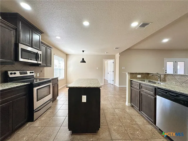 a kitchen with stainless steel appliances granite countertop a refrigerator a sink a stove a microwave and island