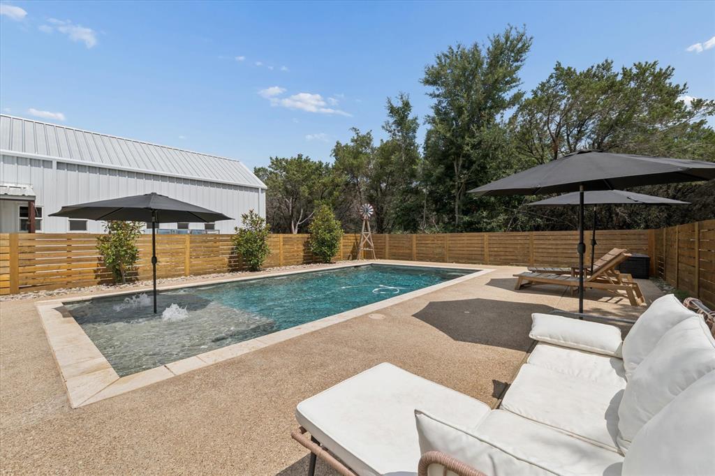 286 Benevolence Way China Spring, TX 76633 - Photo 28 of 37 Rectangular swimming pool featuring a tanning ledge with umbrella stand and water feature, surrounded by a gravel aggregate patio