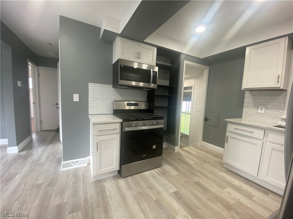 12913 Silver Road Cleveland, OH 44125 - Photo 4 of 23 Kitchen featuring stainless steel appliances, white cabinets, light countertops, light hardwood flooring, and backsplash