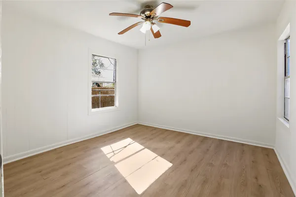an empty room with wooden floor chandelier fan and windows