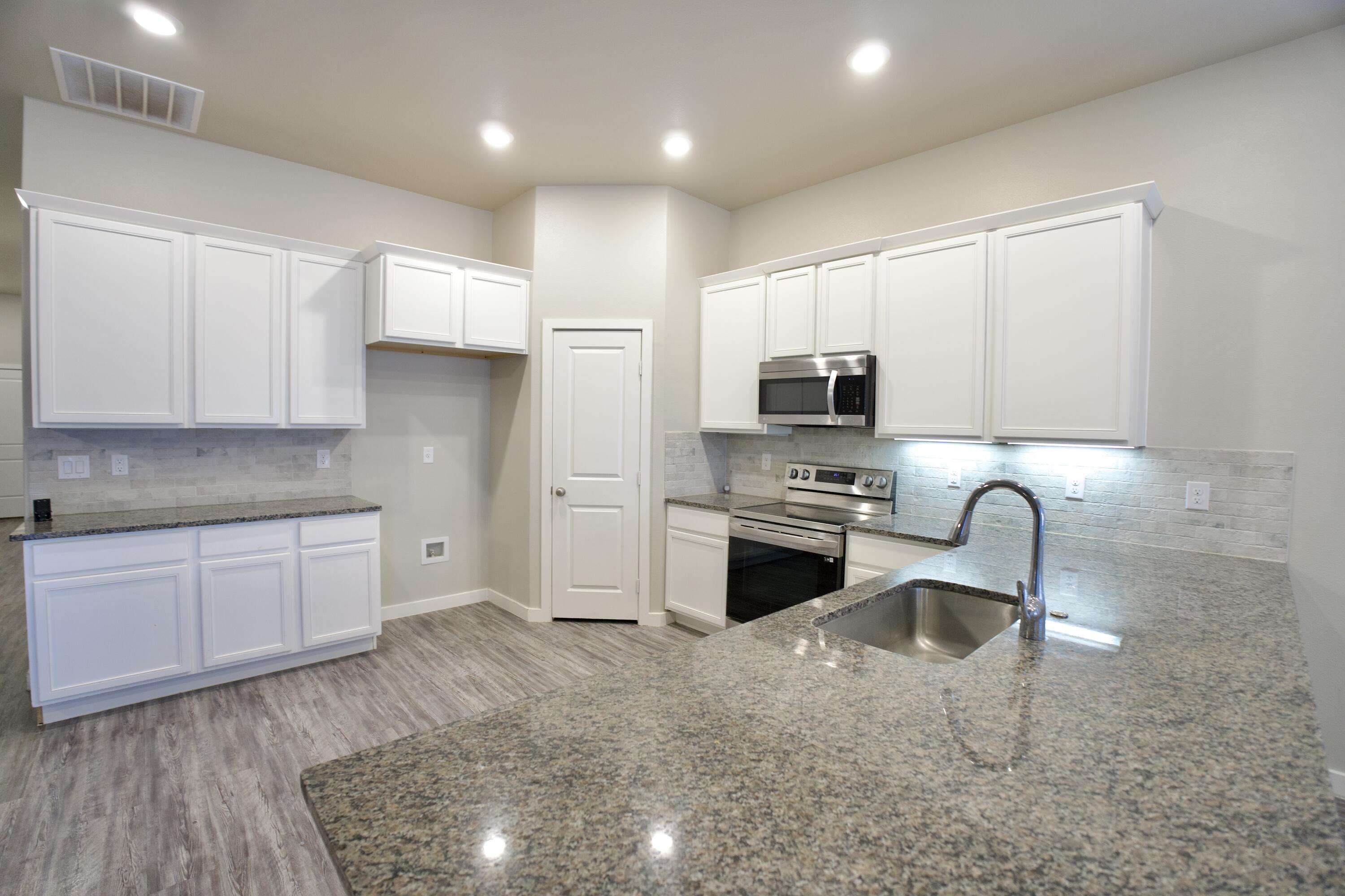 1604 137th Street Lubbock, TX 79423 - Photo 7 of 19 a kitchen with granite countertop a stove a sink and a microwave