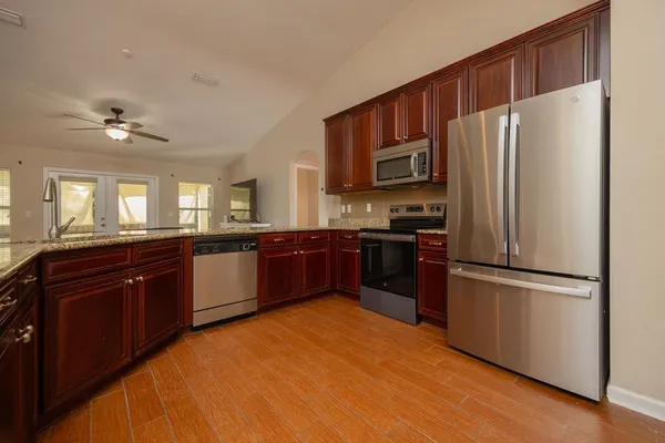 a kitchen with stainless steel appliances granite countertop a refrigerator a sink dishwasher a stove with wooden cabinets and floor