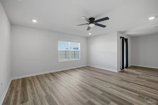 an empty room with wooden floor fan and windows