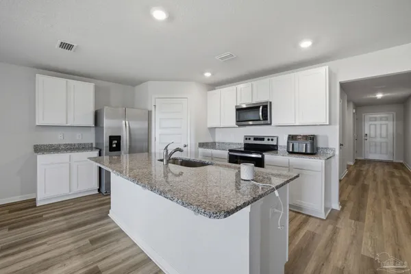 a kitchen with granite countertop stainless steel appliances a stove a sink a refrigerator a microwave a sink and cabinets