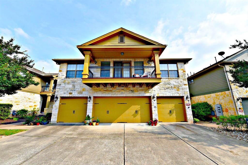 View of front of house with an attached garage, stone siding, a balcony, and driveway