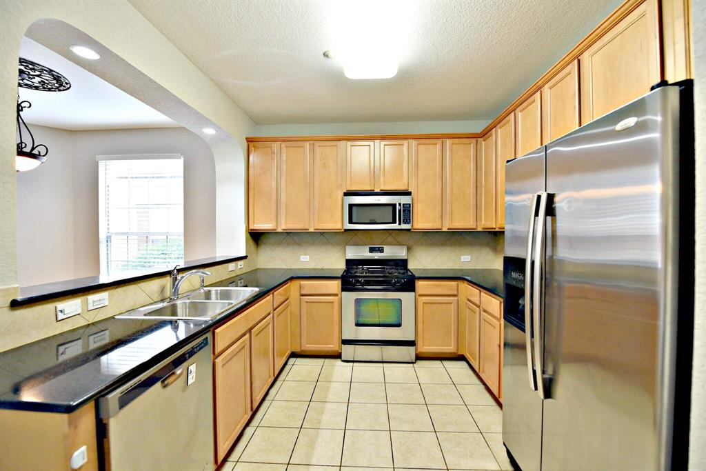 14815 Avery Ranch Boulevard, Unit 702 Austin, TX 78717 - Photo 7 of 19 Kitchen featuring a peninsula, a sink, dark countertops, light brown cabinets, and appliances with stainless steel finishes