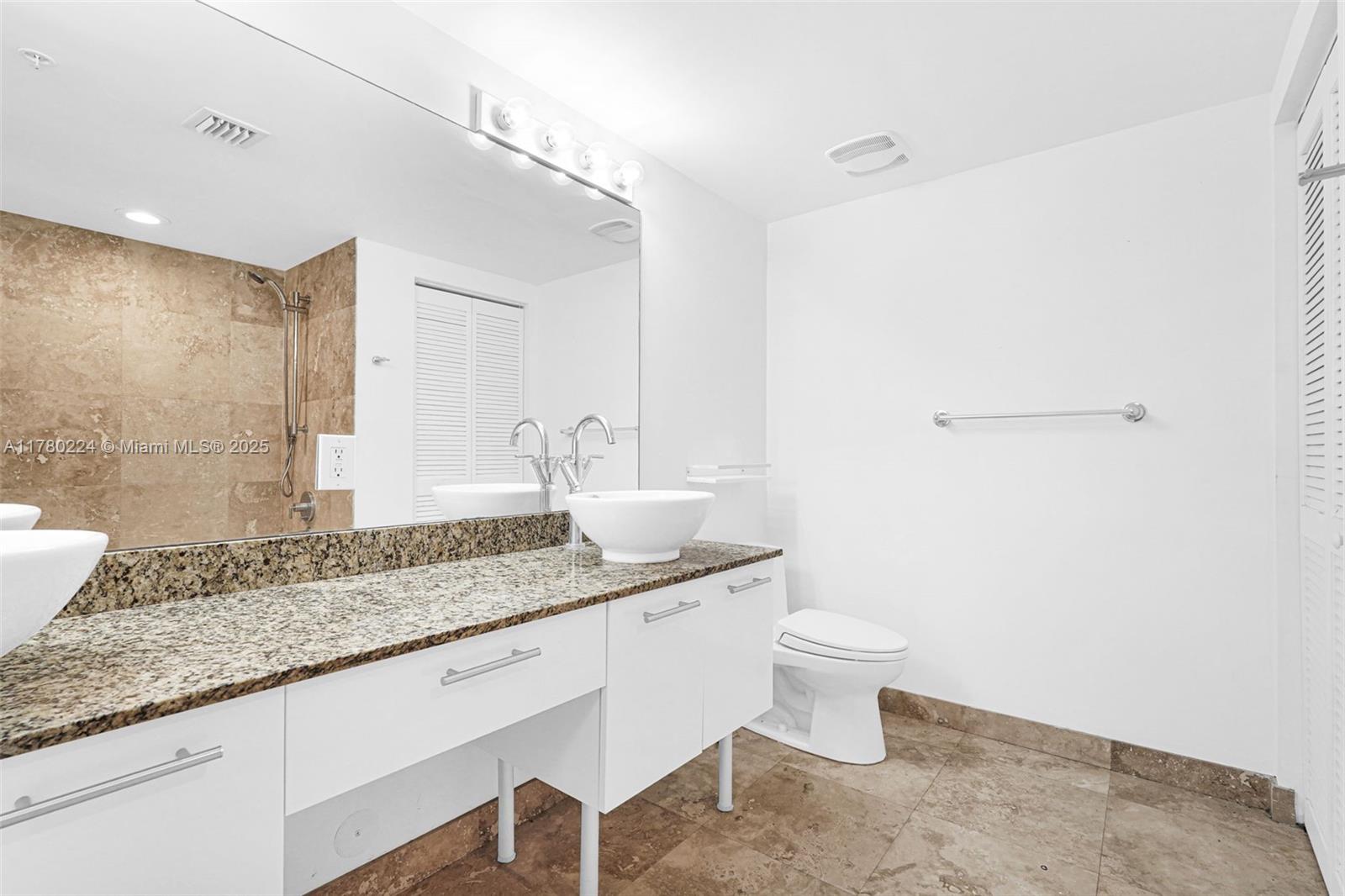 41 Southeast 5th Street, Unit 406 Miami, FL 33131 - Photo 23 of 68 a bathroom with a granite countertop sink a toilet a mirror and vanity