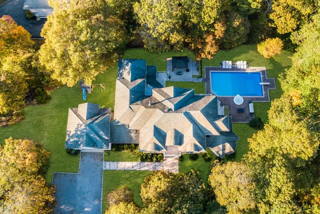 an aerial view of a house with swimming pool and large trees