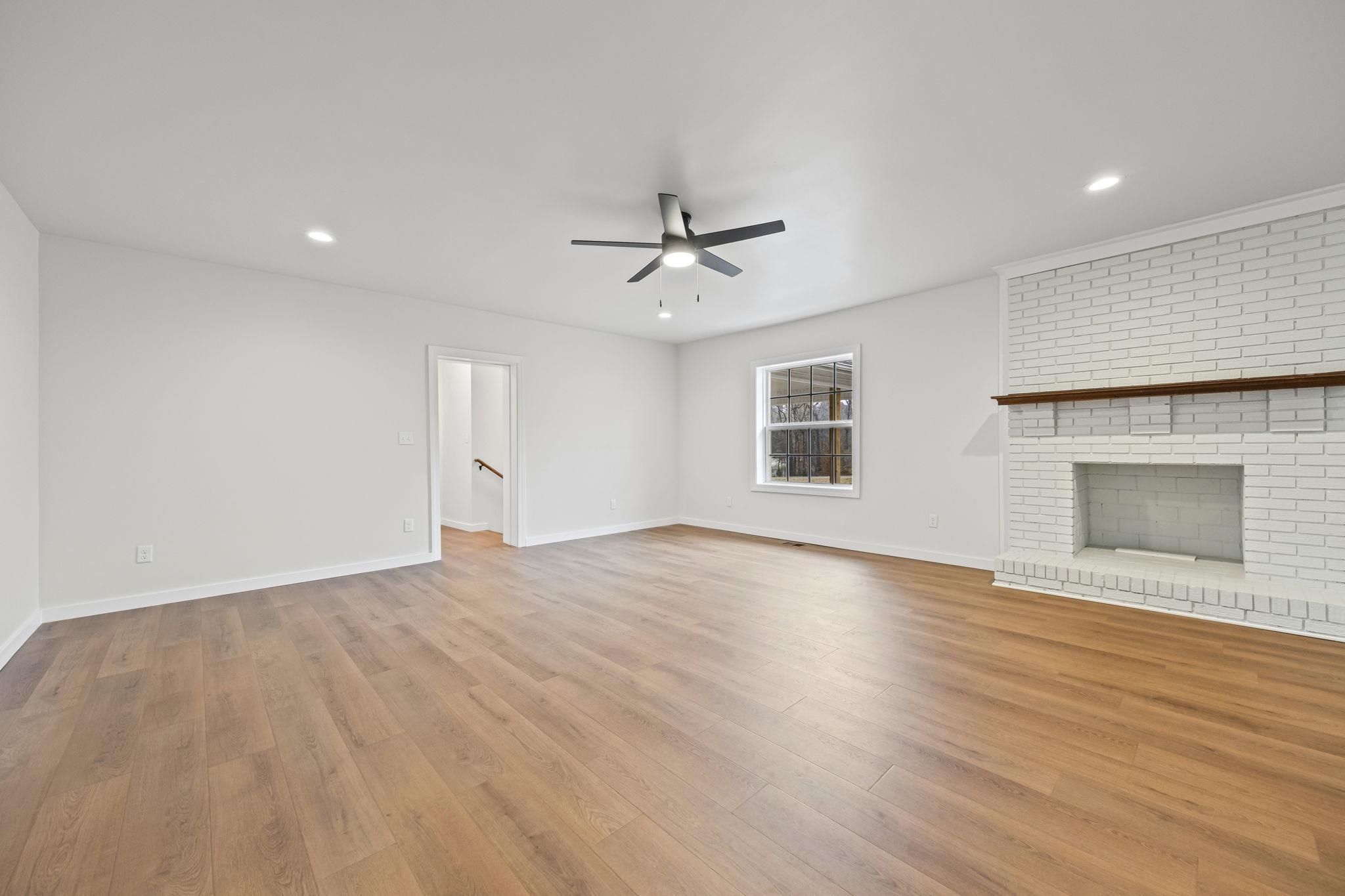 835 Curve Woodville Road Gates, TN 38037 - Photo 6 of 33 an empty room with wooden floor a ceiling fan a fireplace and windows