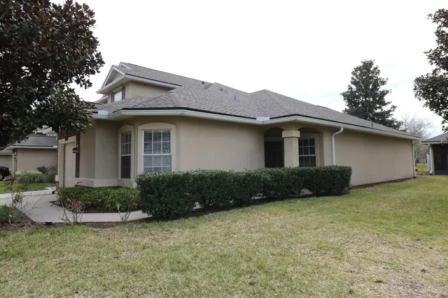 a view of a house with a yard plants and large tree