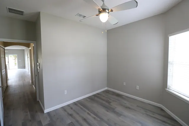 an empty room with wooden floor chandelier fan and windows