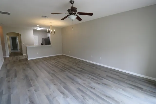 a view of an empty room with wooden floor and a ceiling fan