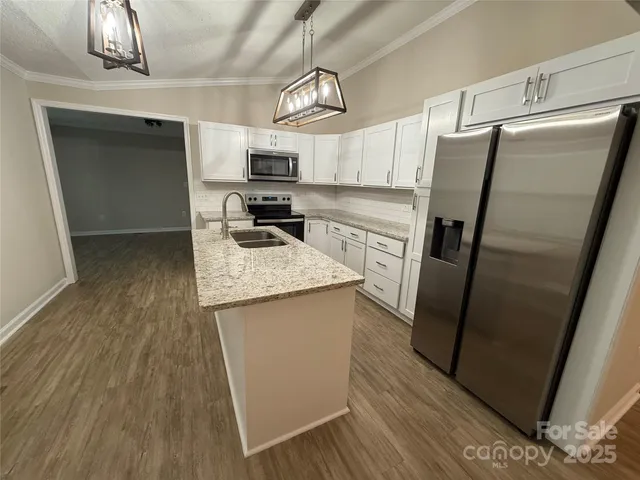 a kitchen with stainless steel appliances a refrigerator a sink dishwasher a stove and white cabinets with wooden floor