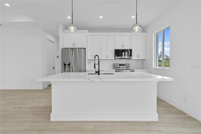 a view of kitchen with kitchen island stainless steel appliances sink cabinets and wooden floor